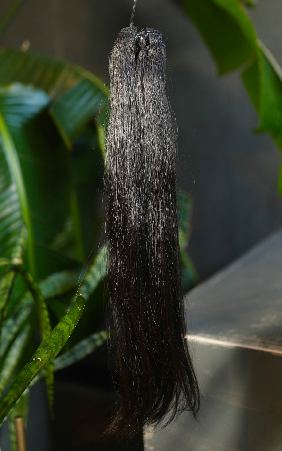 Long dark hair extension bundle displayed against green leaves